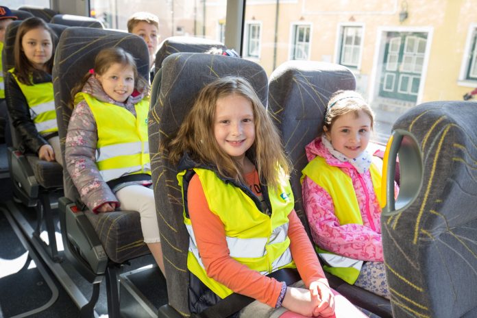 Kinder mit Warnweste im Schulbus