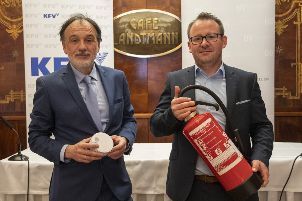 Dr. Armin Kaltenegger mit einem Feuermelder und Dr. Günther Schwabegger mit einem Feuerlöscher vor einem Pressepodium