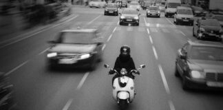 Ein Motorroller im Straßenverkehr zwischen Autos, die mehrspurig in dieselbe Richtung fahren.