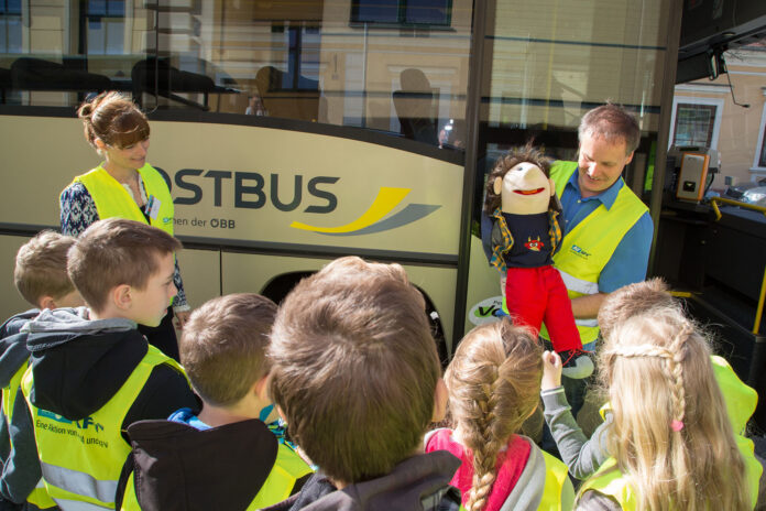 Kinder stehen vor dem Bus bei der Aktion. Ein Mann zeigt Sicherheitsmaßnahmen mit einer Handpuppe vor.