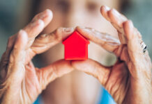 Eine ältere Dame hält ein Spielzeughaus in der Hand