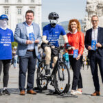Dipl.-Ing. Christian Kräutler (KFV), Mag.a Maria Lesterl (Direktorin der AUVA-Landesstelle Linz) und Leonhard Zauner MLS (Vorsitzender des Landesstellenausschusses) stehen in Linz am Hauptplatz mit einem kopflosen Aktionsmitarbeitenden und einer kopflosen Radfahrer-Puppe.