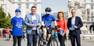 Dipl.-Ing. Christian Kräutler (KFV), Mag.a Maria Lesterl (Direktorin der AUVA-Landesstelle Linz) und Leonhard Zauner MLS (Vorsitzender des Landesstellenausschusses) stehen in Linz am Hauptplatz mit einem kopflosen Aktionsmitarbeitenden und einer kopflosen Radfahrer-Puppe.