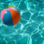 Ein bunter Wasserball in türkis-glitzerndem Poolwasser.