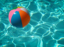 Ein bunter Wasserball in türkis-glitzerndem Poolwasser.