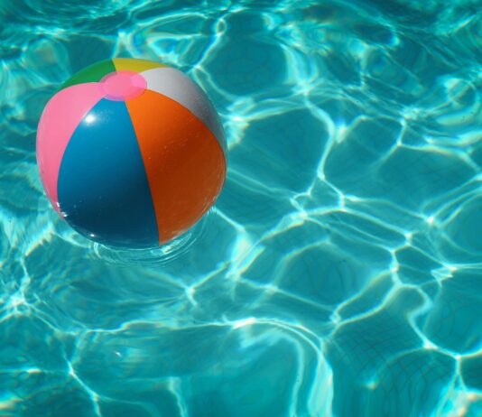 Ein bunter Wasserball in türkis-glitzerndem Poolwasser.