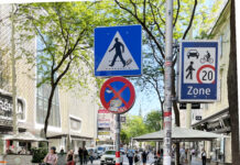 Eine Begegnungszone: Sichtbar sind die Passant*innen und die Schilder für die zu Fuß Gehenden und die begrünte Begegnungszone.