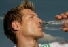 Ein schwitzender Mann im Sportdress, der aus einer Flasche Wasser trinkt.