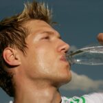 Ein schwitzender Mann im Sportdress, der aus einer Flasche Wasser trinkt.