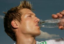 Ein schwitzender Mann im Sportdress, der aus einer Flasche Wasser trinkt.