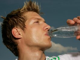 Ein schwitzender Mann im Sportdress, der aus einer Flasche Wasser trinkt.
