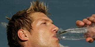 Ein schwitzender Mann im Sportdress, der aus einer Flasche Wasser trinkt.