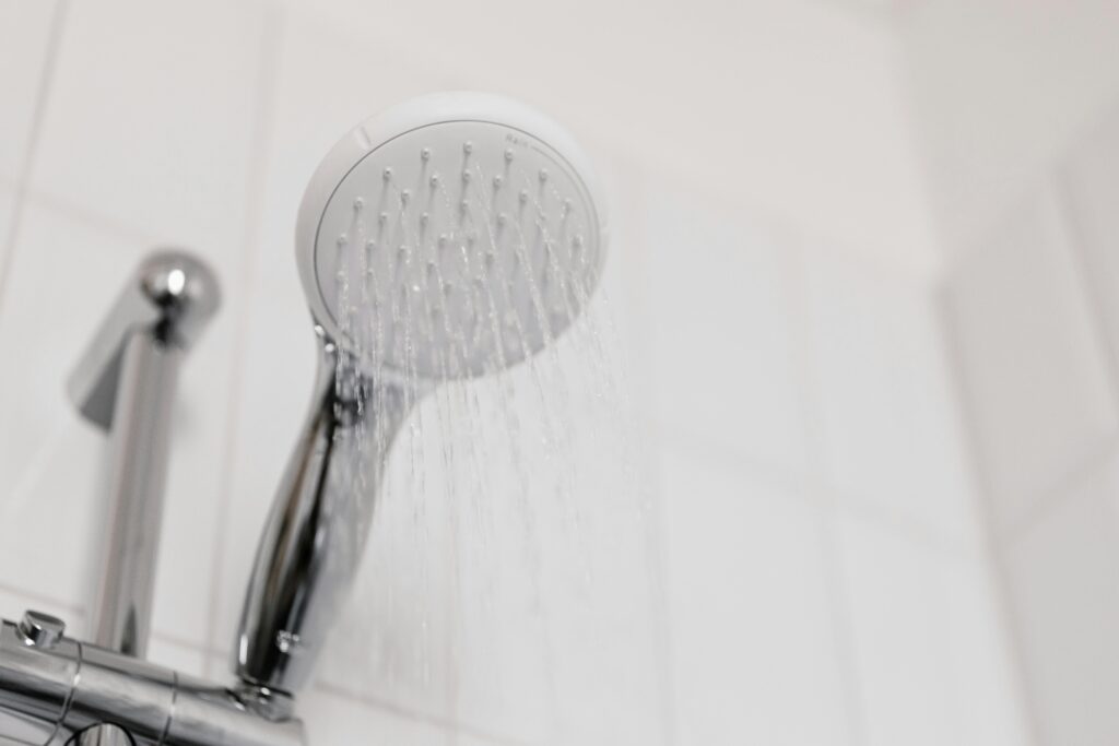 Ein Duschkopf, aus dem Wasser rinnt in einer weiß gefliesten Dusche.