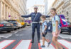 Ein Polizist auf einem Zebrastreifen ermöglicht 2 Schulkindern die sichere Überquerung.