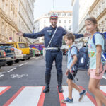 Ein Polizist auf einem Zebrastreifen ermöglicht 2 Schulkindern die sichere Überquerung.