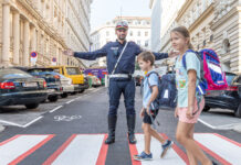 Ein Polizist auf einem Zebrastreifen ermöglicht 2 Schulkindern die sichere Überquerung.