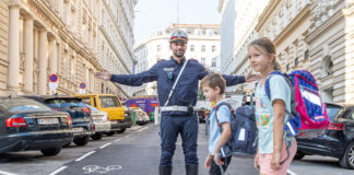 Ein Polizist auf einem Zebrastreifen ermöglicht 2 Schulkindern die sichere Überquerung.