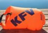 Eine orange Schwimmboje mit KFV-Logo liegt aufgeblasen auf dem Holzsteg vor einem spiegelglatten See.