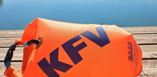 Eine orange Schwimmboje mit KFV-Logo liegt aufgeblasen auf dem Holzsteg vor einem spiegelglatten See.