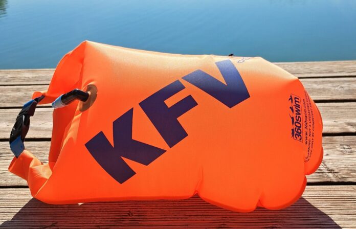 Eine orange Schwimmboje mit KFV-Logo liegt aufgeblasen auf dem Holzsteg vor einem spiegelglatten See.