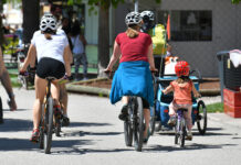 Man sieht Radfahrer*innen von hinten: Kinder wie erwachsene, selbst- sowie mitfahrend, auf einer Straße.