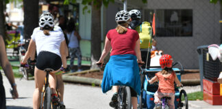Man sieht Radfahrer*innen von hinten: Kinder wie erwachsene, selbst- sowie mitfahrend, auf einer Straße.