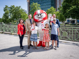 Doris Wendler, Präsidentin des KFV (Kuratorium für Verkehrssicherheit), Mobilitätsminister Peter Hanke, Kult-Maskottchen HELMI, Christian Schimanofsky, Geschäftsführer des KFV und begeisterte Kinder freuen sich auf die Aktion und stehen vor dem Bundesministerium.