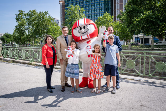 Doris Wendler, Präsidentin des KFV (Kuratorium für Verkehrssicherheit), Mobilitätsminister Peter Hanke, Kult-Maskottchen HELMI, Christian Schimanofsky, Geschäftsführer des KFV und begeisterte Kinder freuen sich auf die Aktion und stehen vor dem Bundesministerium.