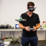 Ein Mann mit VR-Brille lenkt eine Drohne vor sich in einem Raum.