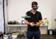 Ein Mann mit VR-Brille lenkt eine Drohne vor sich in einem Raum.