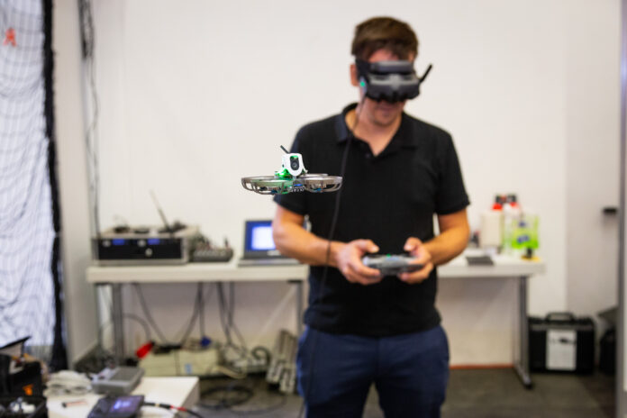 Ein Mann mit VR-Brille lenkt eine Drohne vor sich in einem Raum.