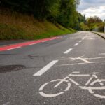 Sicher Radfahren auf der Landstraße: Test neuer Bodenmarkierungen Eine Fahrbahn mit einem breiten Radweg auf der Fahrbahn, einer mittleren Fahrbahn für Autofahrende und einem weiteren Streifen (in rot), der ebenfalls für Fahrradfahrende vorgesehen ist.