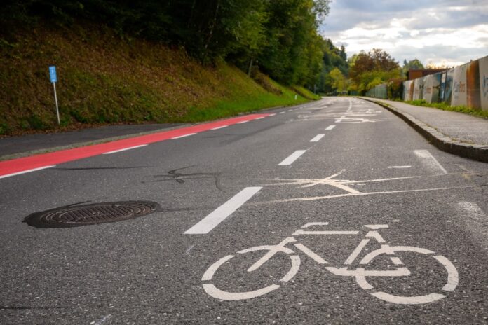 Eine Fahrbahn mit einem breiten Radweg auf der Fahrbahn, einer mittleren Fahrbahn für Autofahrende und einem weiteren Streifen (in rot), der ebenfalls für Fahrradfahrende vorgesehen ist.