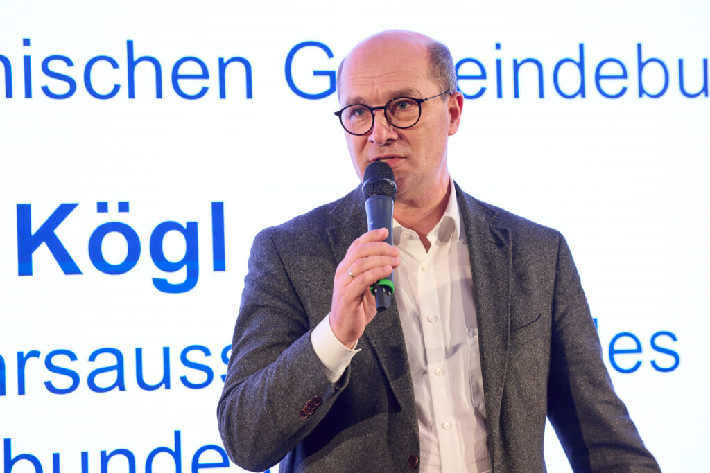 Ein Mann in Hemd und Anzug und mit Brille hält ein Mikrofon in der Hand.