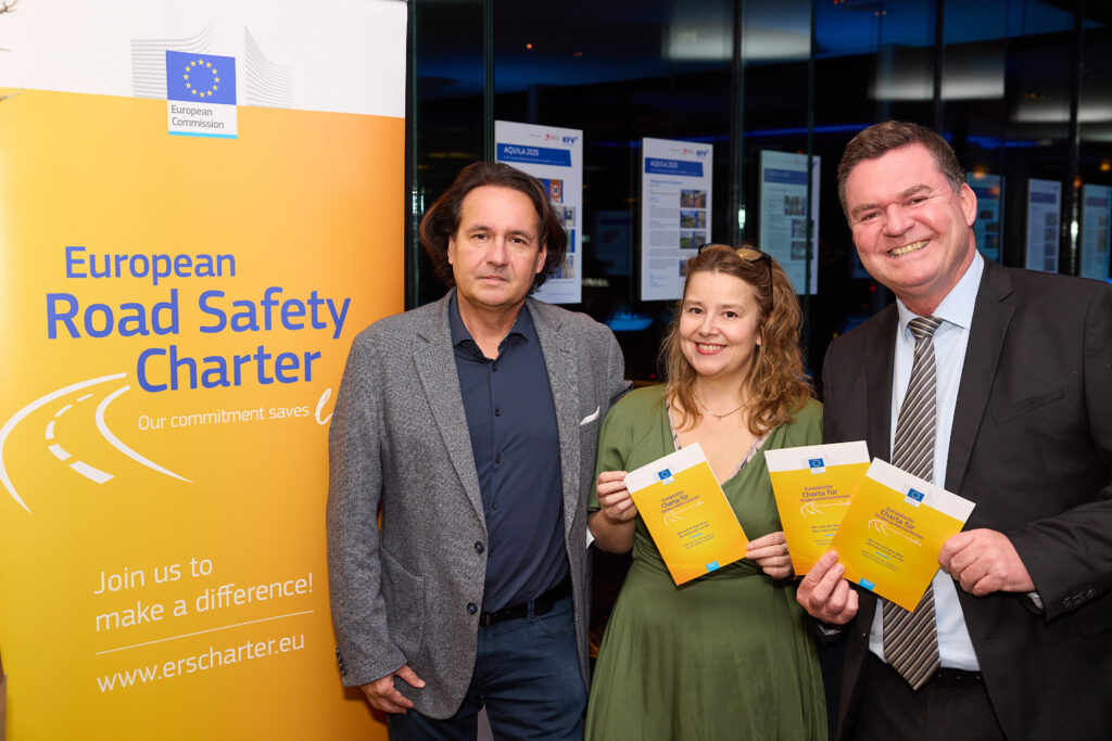 Gerald Furian, Rosa Guevara und Christian Kräutler (KFV) stehen neben einem Roll-Up für die European Road Safety Charter und halten Informationsbroschüren lächelnd in die Kamera.