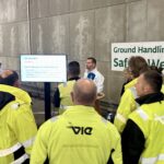 13 Workshops, 905 Teilnehmende: Flughafen Wien setzt starkes Zeichen gegen Ablenkung im Straßenverkehr Eine Gruppe Mitarbeitende des Wiener Flughafens stehen zusammen und hören sich einen Vortrag an.