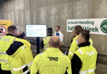 Eine Gruppe Mitarbeitende des Wiener Flughafens stehen zusammen und hören sich einen Vortrag an.