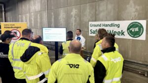 Eine Gruppe Mitarbeitende des Wiener Flughafens stehen zusammen und hören sich einen Vortrag an.