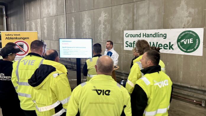 Eine Gruppe Mitarbeitende des Wiener Flughafens stehen zusammen und hören sich einen Vortrag an.