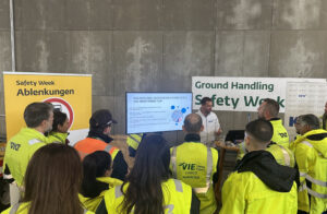 Eine Gruppe Mitarbeitende des Wiener Flughafens stehen zusammen und hören sich einen Vortrag an.