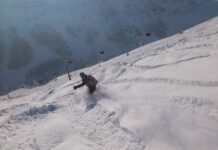 Eine Person fährt im winterlichen Tiefschneegelände bergab. Im Hintergrund sieht man einen Gondellift.