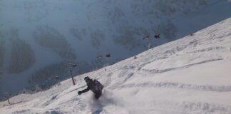 Eine Person fährt im winterlichen Tiefschneegelände bergab. Im Hintergrund sieht man einen Gondellift.