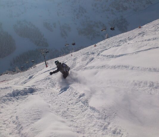 Eine Person fährt im winterlichen Tiefschneegelände bergab. Im Hintergrund sieht man einen Gondellift.