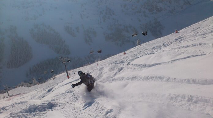 Eine Person fährt im winterlichen Tiefschneegelände bergab. Im Hintergrund sieht man einen Gondellift.