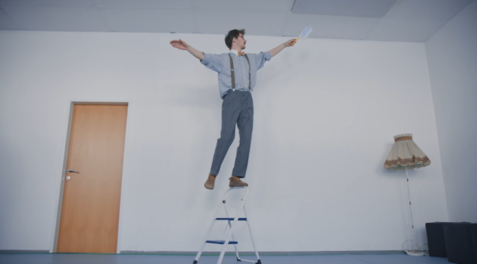 Gefährliche Balanceakte beim Frühjahrsputz Ein Mann balanciert auf dem Griff einer Trittleiter und hält dabei einen Staubwedel in der Hand.