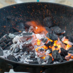 In einem Kugelgrill sieht man lodernde Grillkohle und Flammen.