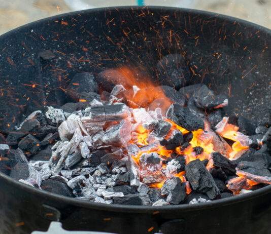 In einem Kugelgrill sieht man lodernde Grillkohle und Flammen.
