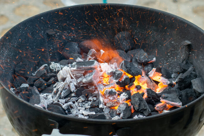 In einem Kugelgrill sieht man lodernde Grillkohle und Flammen.