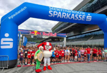 KFV mit Helmi beim Sparkassen Businesslauf 2026 Kinder und Jugendliche stehen beim Businesslauf 2026 am Red Bull Ring unter einem blauen Startbogen der Steiermärkischen Sparkasse, davor zwei Maskottchen.