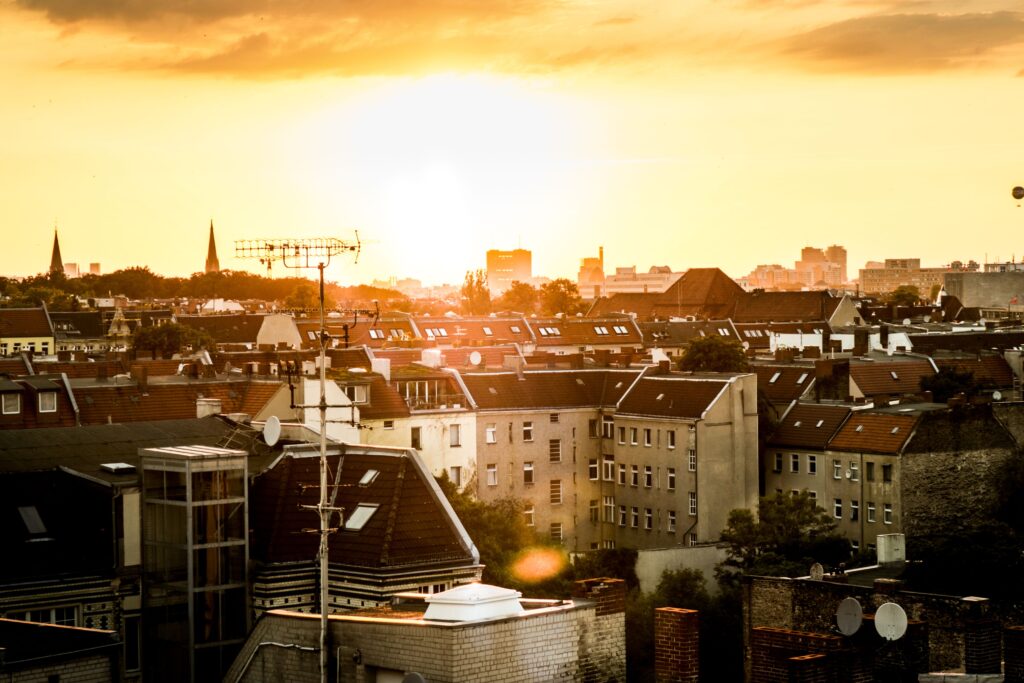 Eine Aufnahme einer Stadt aus der Vogelperspektive, die in das Licht einer am Himmel stehenden Sonne getränkt ist.